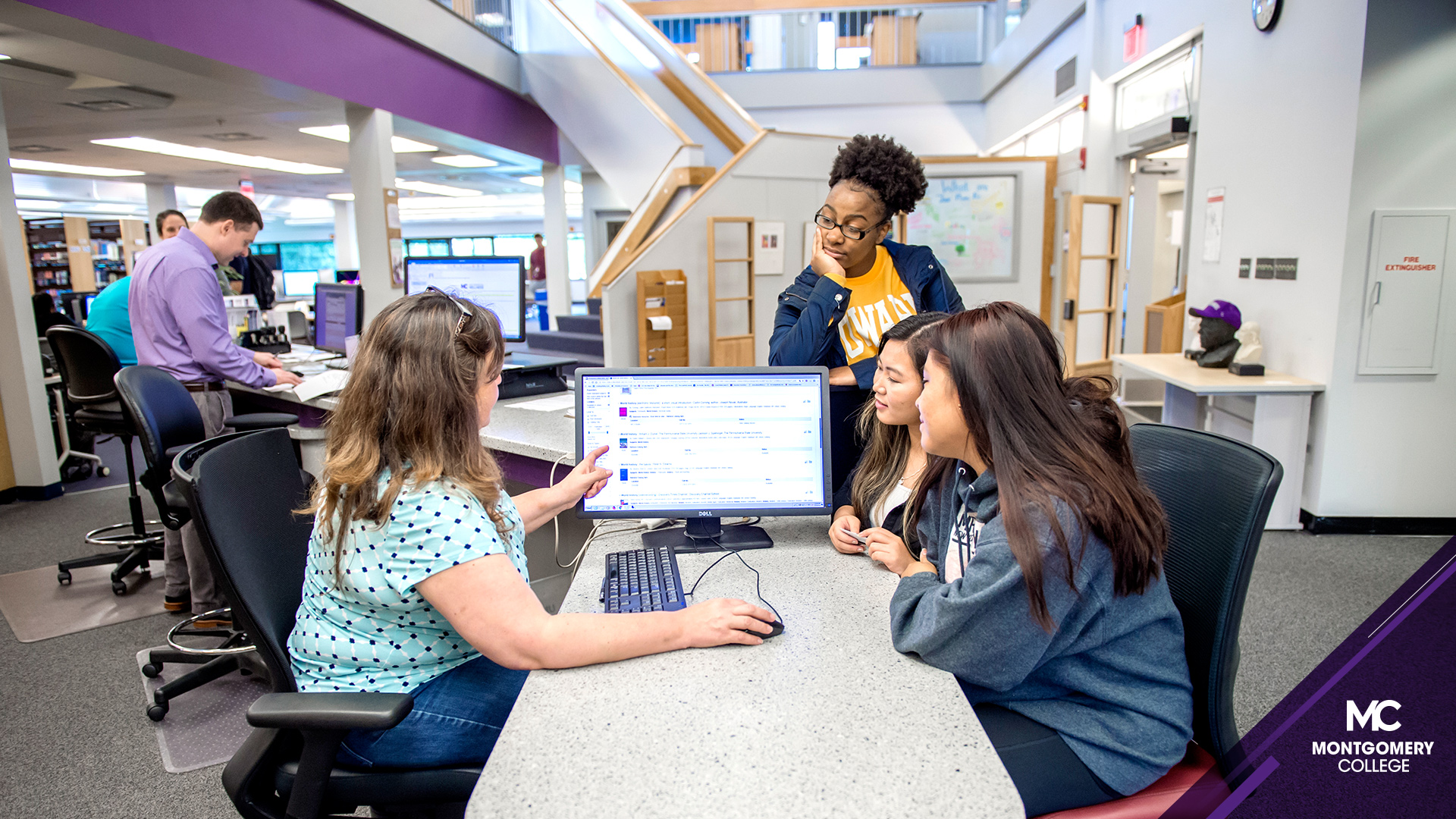 MC Germantown校区-三个学生和一个图书管理员在图书馆的电脑前。